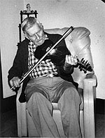 Henry Reed in an armchair, playing the fiddle