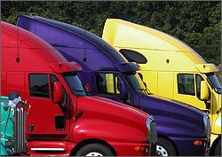 Photo of the cabs of three brightly colored trucks lined up one in front of the other.  The trucks are red, blue, and yellow.