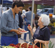 Photo of a man and an older woman looking at strawberries at a market.