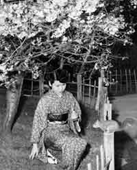 Photo: woman in a kimono kneeling to feed a squirrel.