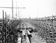 A ship mast and a long row of wood frames stacked vertically.