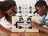 Two students smile as they look into microscopes