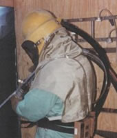 A worker wearing protective equipment while abrasive blasting.