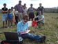 Photo of Jill Bruning entering data with small group standing behind her in a  farmer's field