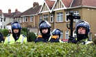 Police personnel stand behind a hedge