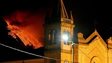 Mount Etna erupts in the background and a church is seen in the foreground. 