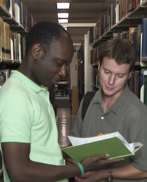 Student slook at a book in the library stacks.