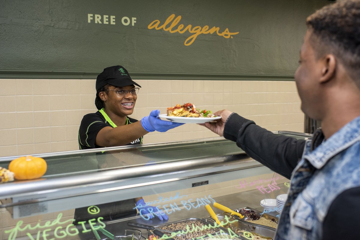 Photo of Kitchen West employee handing a plate of food to a customer.