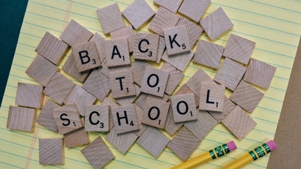 A photograph of scrabble tiles spelling out “back to school” on top of a yellow notepad.