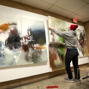 Art student hanging paintings in a campus art gallery