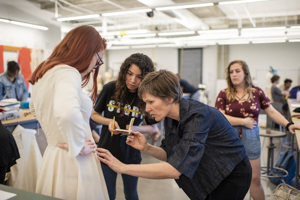 Photo of fashion design student and faculty member work to make adjustments to a garment during a costume fitting.