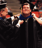 Happy graduate receiving master's hood at commencement