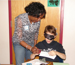 Student learns how to use a signature guide to write his name under blindfold.