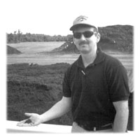 Photo of Evgeniy Lobanov holding mulch with mulch manufacturing site in the background