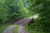 photograph of the gravel auto tour road at the Big Oaks National Wildlife Refuge, Madison, Indiana, showing a gravel road going through a tall oak forest. The road crosses a bridge about half way along the route.