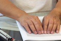 close up on a blind person's hands reading Braille and a folded up cane