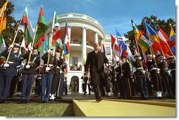 Flying flags from countries contributing to the fight against terrorism, President George W. Bush approaches the podium on the six-month anniversary of the September 11th Attacks on the South Lawn. "We have come together to mark a terrible day, to reaffirm a just and vital cause, and to thank the many nations that share our resolve and will share our common victory," said the President in his remarks.  White House photo by Paul Morse