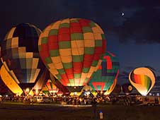 Colorful balloons light up for the Balloon Glow event at the International Balloon Fiesta as the moon peeks from behind the clouds.