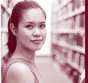 young woman reading book between rows of bookshelves in library