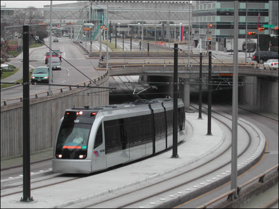 A sleek silver train rounds a bend beneath a bridge