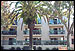 [Photo: Palm trees sway in front of apartment building with balconies]