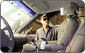 Photo of the inside of a car with bright lights shining through the windshield. A man wearing protective eye wear adjusts a human form made of metal and wires.