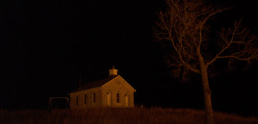 Lower Fox Creek Schoolhouse lit by the light of a prairie fire