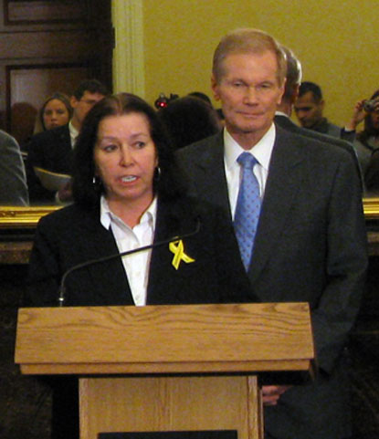 Christine Levinson speaks from a podium at a press conference on a resolution introduced by U.S. Sen. Bill Nelson, right.