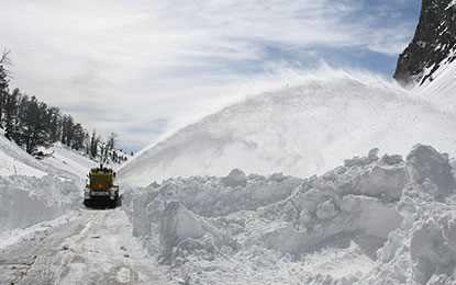 Snow sprays from a plow on deeply snow covered park road.