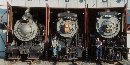 Three steam locomotives are visible in the doors of a roundhouse.