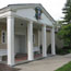 Main entrance to the yellow-brick Presidential Library and Museum, with columns and US flags.