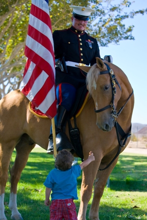 A US Marine Corps officer greets a young child while riding a mustang from BLM's wild horse and burro program.