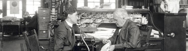 Thomas Edison sitting at his desk talking with an employee.