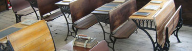 Wooden-topped pupils' desks furnish the inside of a one-room schoolhouse.