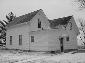 White two-story farmhouse with a double-gabled roof in the snow.