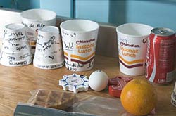  image of styrofoam cups, soda can, an egg, and an orange on a table 