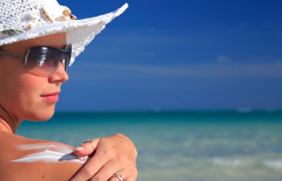 Image of woman wearing sun hat and sunglasses, and applying sunscreen