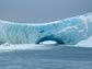 Photo of a person standing underneath a natural ice arch in Antarctica.