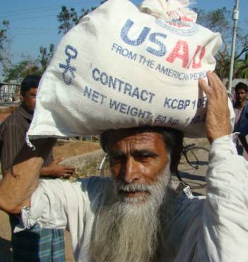 Photo of a Bangladeshi man carrying four, oil, and peas on his head in a USAID sack. Location: Patharghata Upazila, Borguna. Photo: CARE