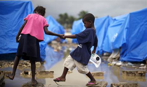 Image: Children cross a puddle of water after heavy rains at a makeshift tent camp in Cite Soleil in Port-au-Prince