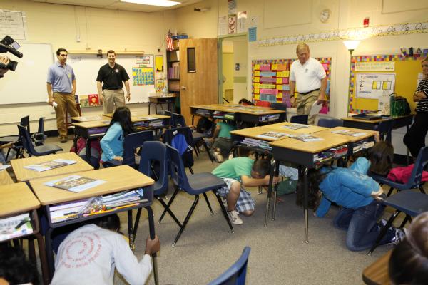 Students practice earthquake safety by getting under their desks.