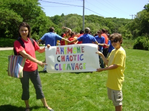 The banner held by Embryology course TA Elke Ober and a young assistant gives a clue what the students are doing: the “chaotic cleavage dance”! The blue T-shirts are the egg's ectoderm, red are the mesoderm, and yellow are the endoderm. Photo by Beth Liles