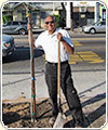 Photograph of a man standing near a tree and holding a shovel.