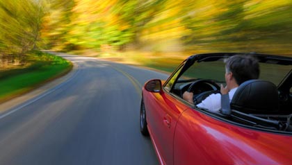 man driving a red convertible down a windy road in summer