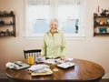 Senior woman smiles while standing at table covered by bills and calculators