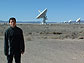 Young man stands in front of a row of white telescopes.