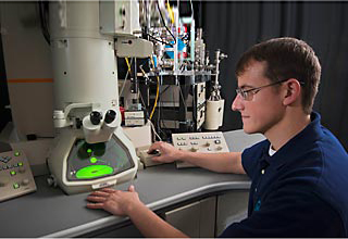 Sandia materials scientist sits in front of the in situ ion irradiation TEM.