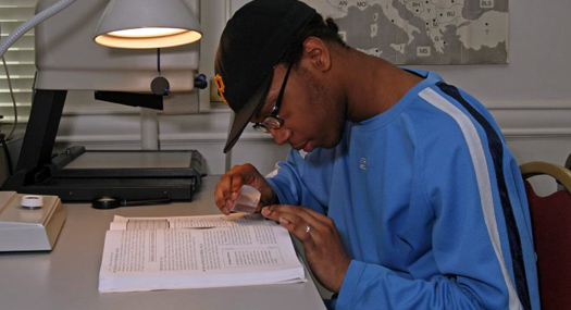 A young man reads a book with a magnifier