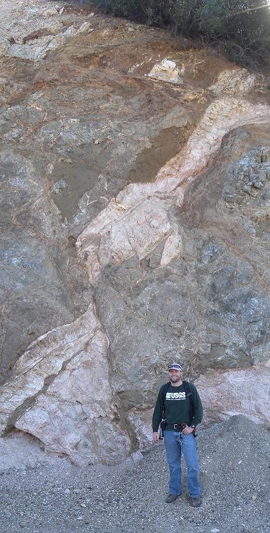 Robert Leeper standing in front of an exposed cliff face showing various layers of rock, particularly a clear fault line running through the center of the rock formation.