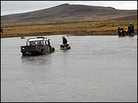 An ATV driver attaches a chain to an expedition truck stuck in a river.